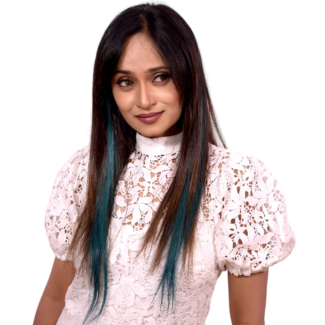 Woman with long dark hair and blue streaks wearing a white lace top on a white background